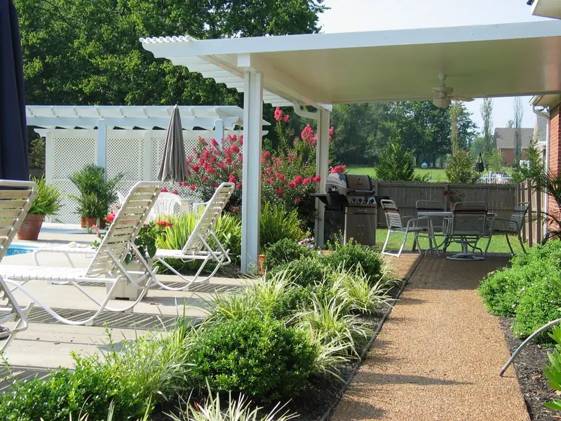 White aluminum patio cover beside a pool, with a gravel path and landscaping